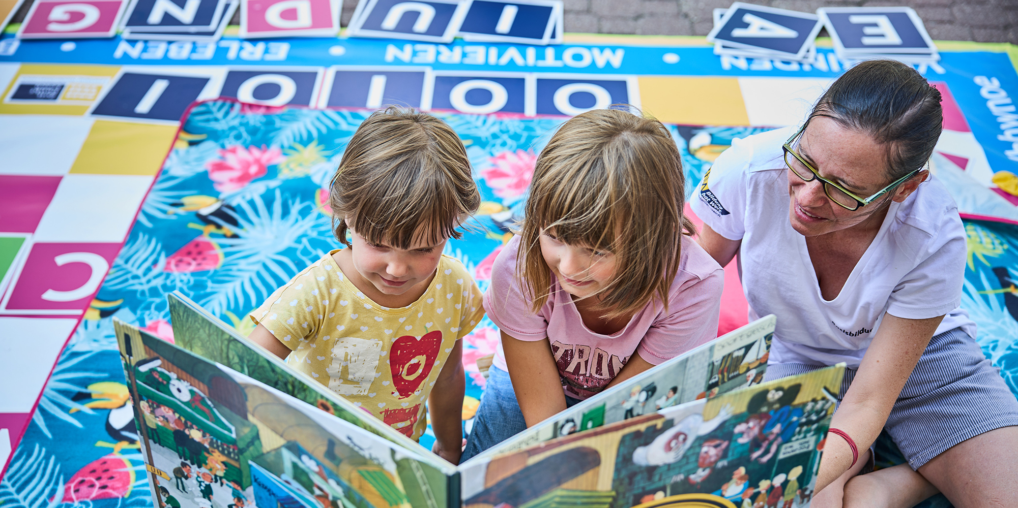Zwei Kinder und einen Erwachsenen sitzen am Boden und lesen in einem Buch